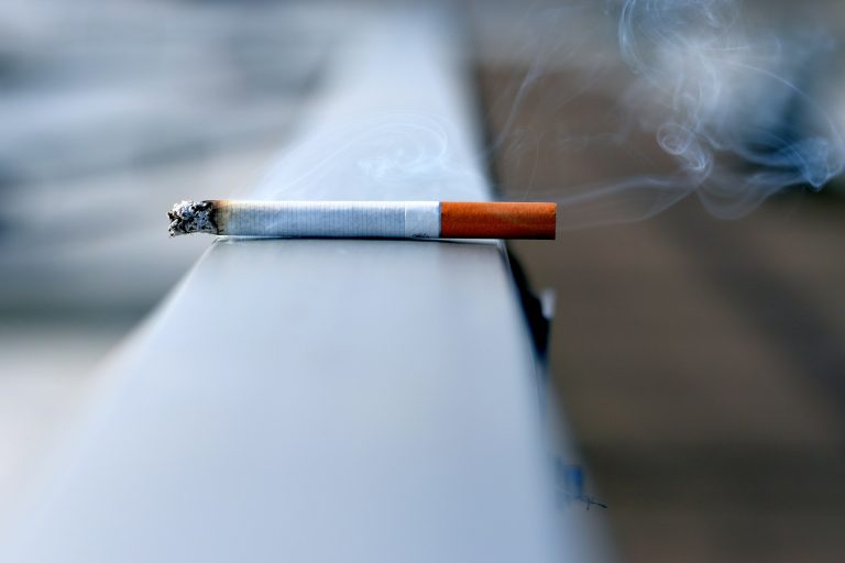 A lit cigaretta sits on a metal handrail